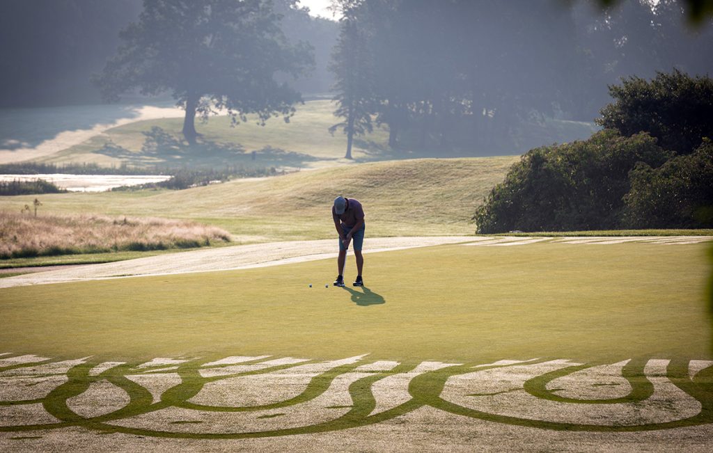 A single golfer set up a tee on a well landscaped golf course.