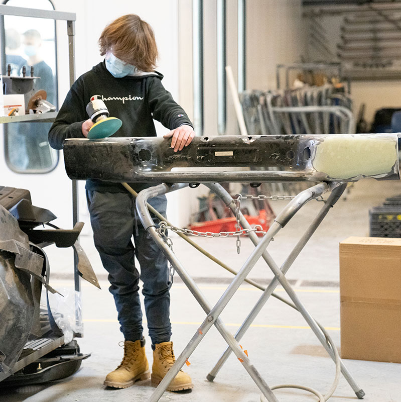 A student uses a grinder on a fender.