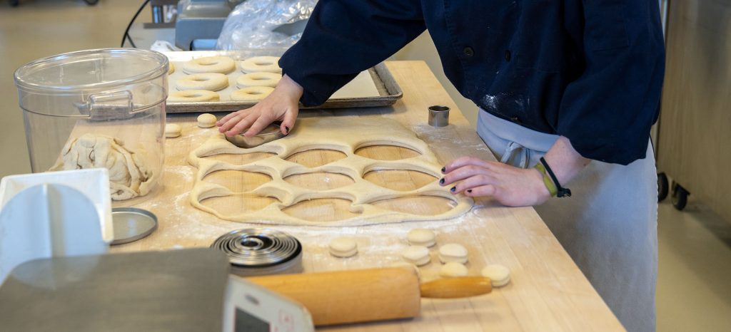 A student cuts out cookies from a sheet of dough.