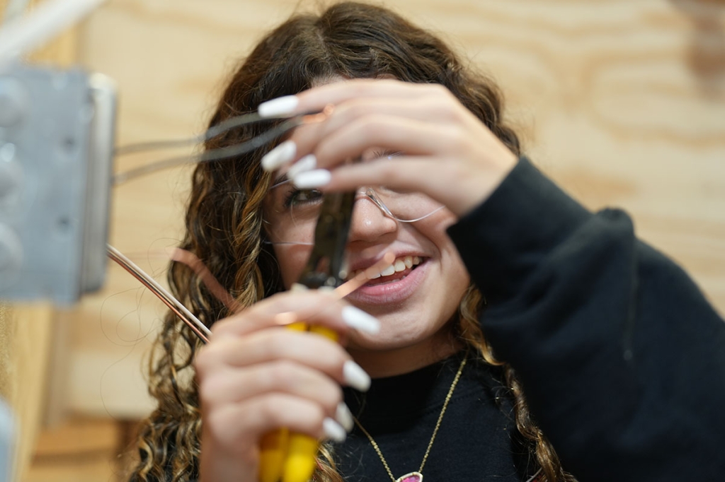 A female student wires an electrical box.