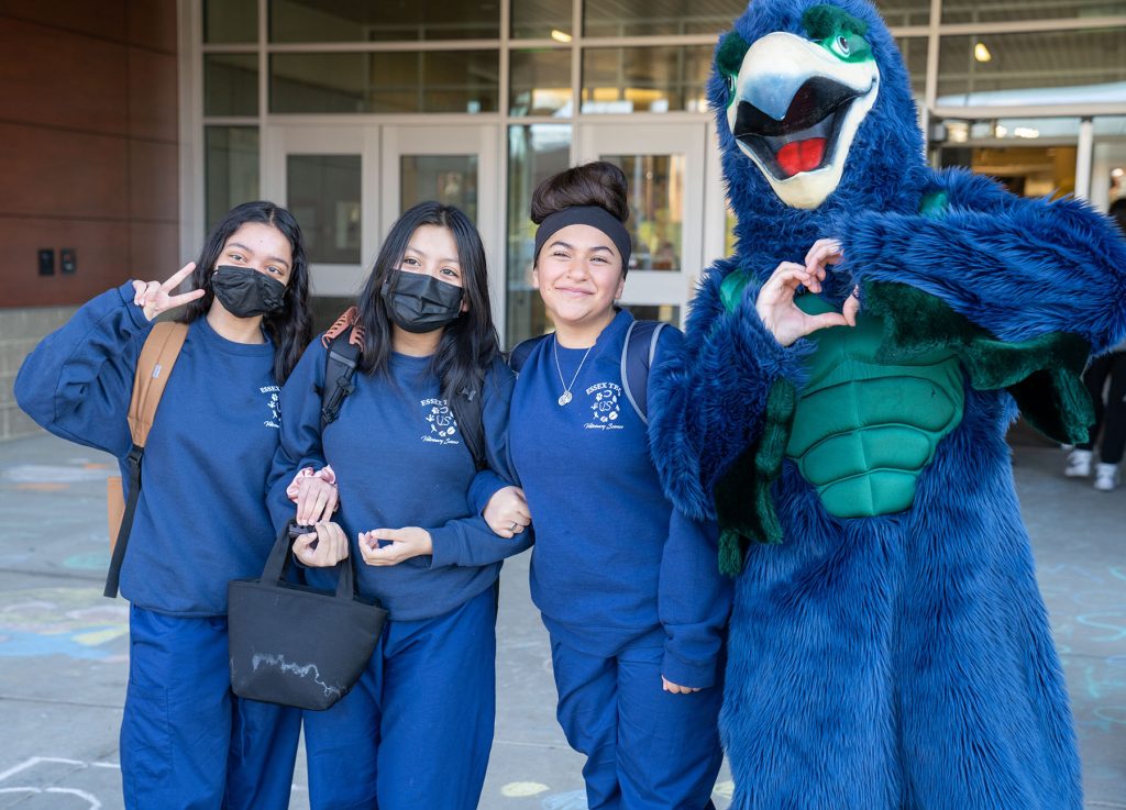 Three students stand next to the school hawk mascot.