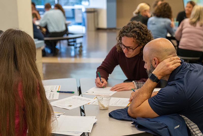 Teachers sit around a table filling out forms.