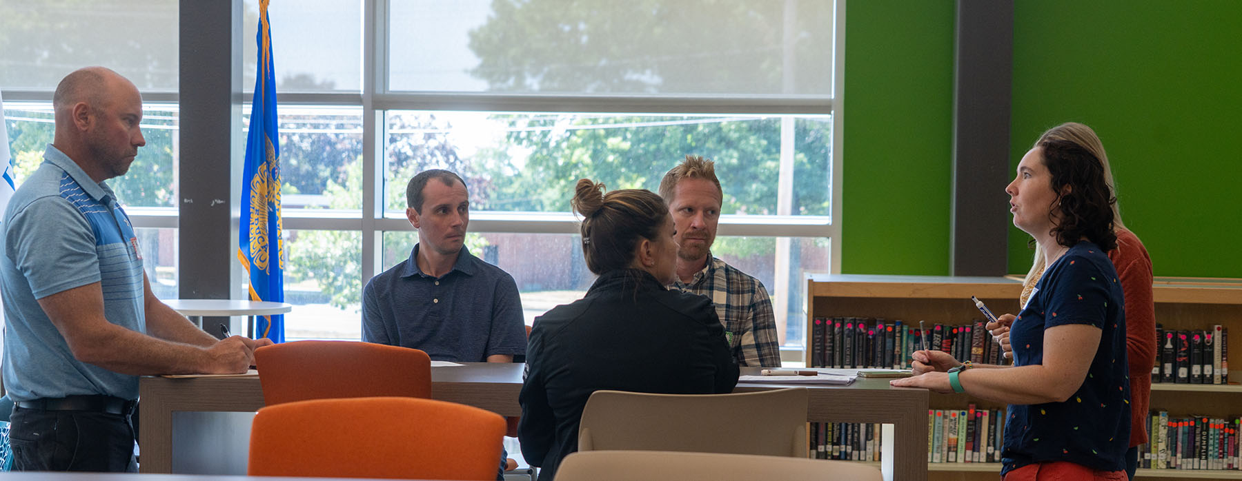 Teachers sitting around a conference table look at and react to a speaker at the end of the table.